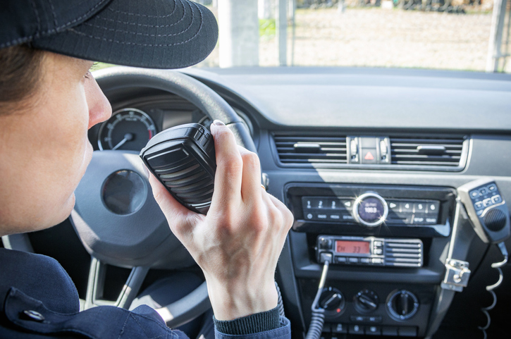 Microphone of a radio or walkie-talkie in the hand of a female police officer in her patrol police car.