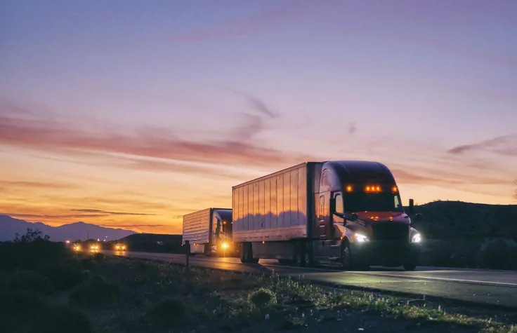 Large semi truck hauling freight on the open highway in the western USA under an evening sky.